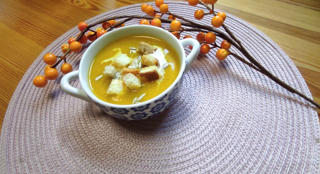 Krem z pieczonej dyni z dekoracją jesienną podany z grzankami i kleksem śmietany